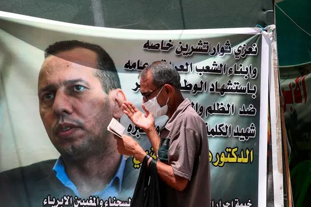 A protester prays by a poster showing Hisham al-Hashimi an Iraqi analyst who was a leading expert on the Islamic State and other armed groups who was shot dead in Baghdad on Monday as demonstrators gather to protest against armed Iranian-backed militias, in Baghdad, Iraq, Sunday, July 12, 2020. (AP Photo/Khalid Mohammed)