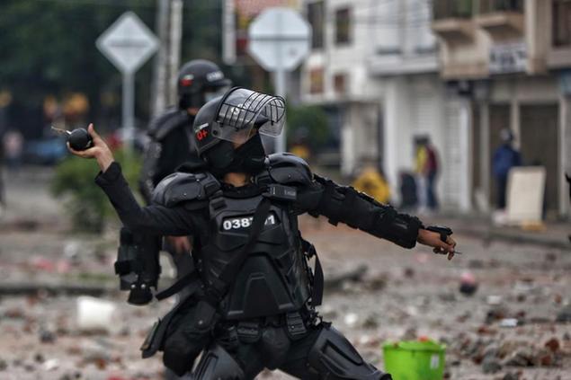 A police officer winds up to throw a stun grenade at protesters during a national strike against tax reform in Cali, Colombia, Monday, May 3, 2021. Colombia's President Ivan Duque withdrew the government-proposed tax reform on Sunday. (AP Photo/Andres Gonzalez)