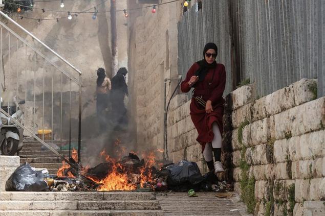 Una donna palestinese cammina accanto ai rifiuti incendiati durante gli scontri con la polizia israeliana nel giorno di Pasqua (Ilia Yefimovich/picture-alliance/dpa/AP Images)