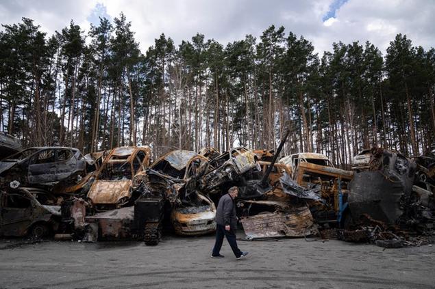 A man walks past a storage place for burned armed vehicles and cars, in the outskirts of Kyiv, Ukraine, Monday, April 11, 2022. (AP Photo/Evgeniy Maloletka)