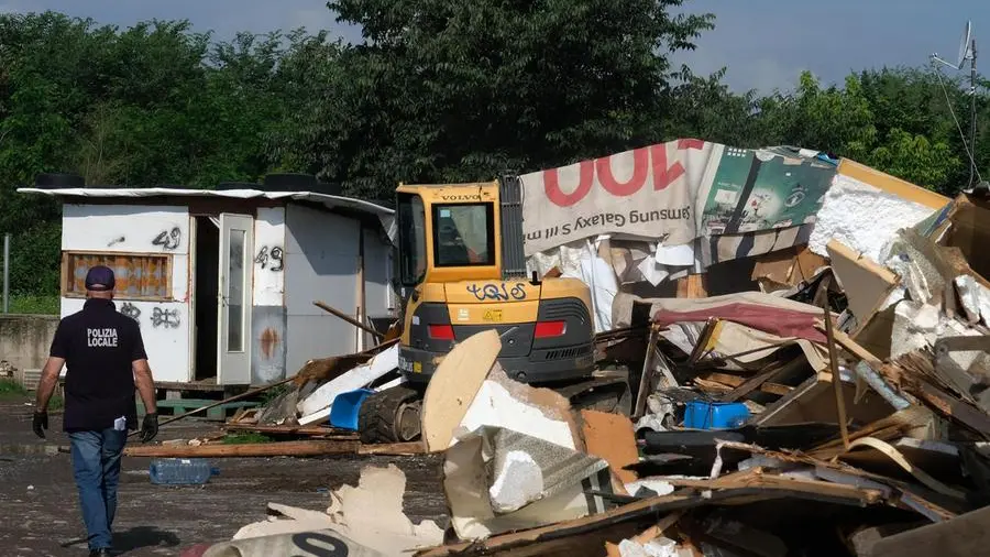 Sgomberi e distruzione di baracche in una zona marginale della città, con persone che si spostano con sacchi di oggetti