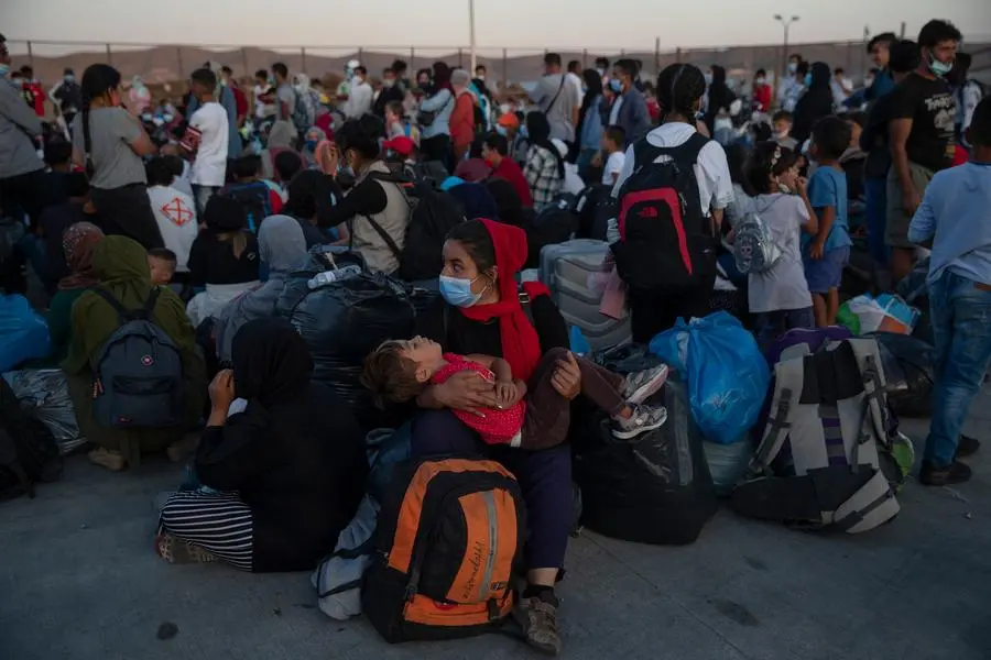 Refugees and migrants wearing protective masks to help curb the spread of coronavirus wait to board buses after their arrival at the port of Lavrion, about 75 kilometers (48miles) south of Athens, Tuesday, Sept. 29, 2020. Greek authorities have moved nearly 1,000 asylum-seekers from eastern Aegean islands to the mainland as part of efforts to improve conditions in overcrowded island camps. Most of the people on a ferry that docked Tuesday at Lavrio, near Athens, were from a temporary facility hastily built on the island of Lesbos to replace a squalid camp that angry residents burned down three weeks ago.(AP Photo/Petros Giannakouris)