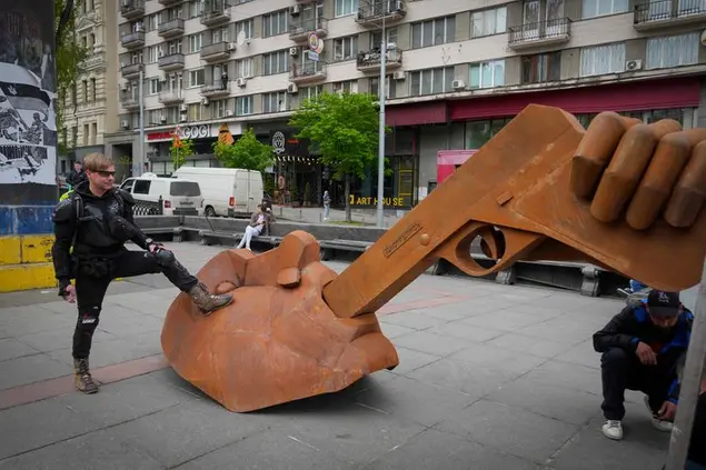 A man puts his foot on sculpture of Russian President Vladimir Putin with a gun in the mouth and writing \\\"Shoot yourself\\\" during its installation in central Kyiv, Ukraine, Saturday, May 7, 2022. (AP Photo/Efrem Lukatsky)