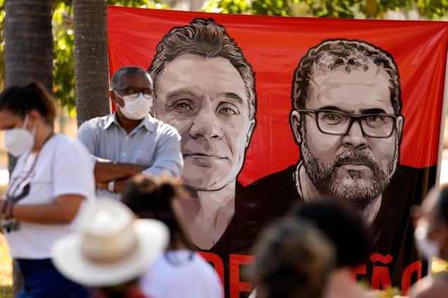 Workers of the National Indian Foundation, FUNAI, stand next to a banner with images of missing Indigenous expert Bruno Pereira, right, and freelance British journalist Dom Phillips, during a vigil in Brasilia, Brazil, Monday, June 13, 2022. Brazilian police are still searching for Pereira and Phillips, who went missing in a remote area of Brazil's Amazon a week ago. (AP Photo/Eraldo Peres)