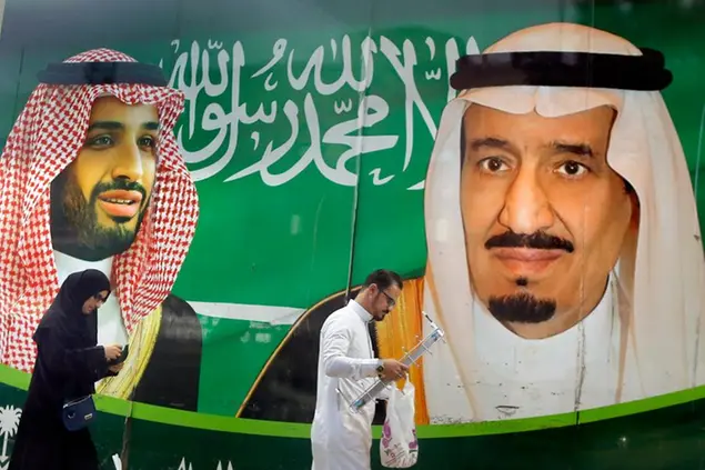 People walk past a banner showing Saudi King Salman, right, and his Crown Prince Mohammed bin Salman, outside a mall in Jiddah, Saudi Arabia, Saturday, March 7, 2020. (AP Photo/Amr Nabil)