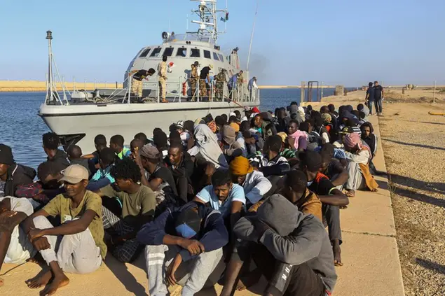 Migranti seduti nel porto di Khoms, in\\u00A0Libia, dopo essere stati sbarcati da una motovedetta della guardia costiera libica (Foto LaPresse)