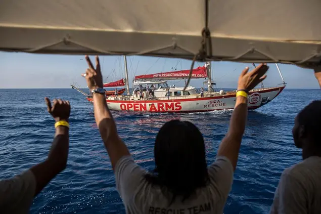 Migrants aboard the Open Arms aid boat, of Proactiva Open Arms Spanish NGO, gesture towards a boat of the Astral Aid vessel, as the ship approaches the port of Barcelona, Spain, Wednesday, July 4, 2018. The aid boat sailed to Spain with 60 migrants rescued on Saturday in waters near Libya, after it was rejected by both Italy and Malta. (AP Photo/Olmo Calvo)