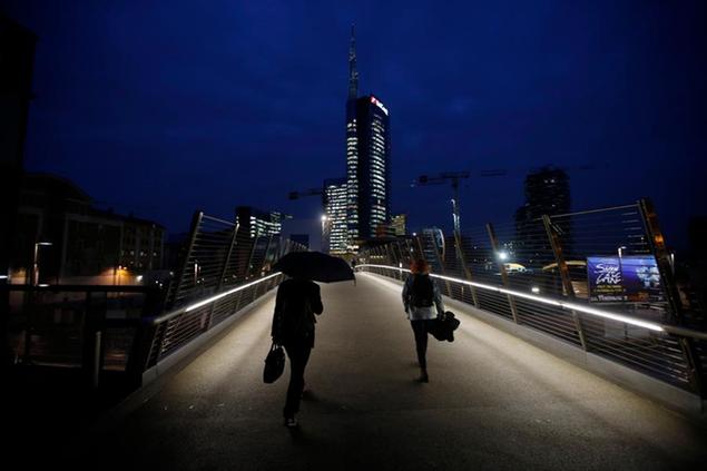 FILE- In this file photo dated Tuesday, Nov. 11 , 2014, people walk on a bridge which leads to business center and the Unicredit headquarters building, center, in Milan, Italy. The recent Europe-wide health check on banks is producing results for Italy, whose top two lenders on Tuesday posted a strong rise in quarterly profits after cleaning up their finances in anticipation of the test. While nine smaller Italian banks failed the test, putting a negative spotlight on Italy's failure to generate economic growth, UniCredit and Intesa SanPaolo, the country's two biggest banks, passed with strong marks. Ahead of the test, the two banks cleaned out their books by writing off bad loans, a painful process that seems to be paying dividends. On Tuesday, both reported profits in the three months ending Sept. 30 more than doubling, early signs of recovery in the banking sector. (AP Photo/Luca Bruno, FILE)