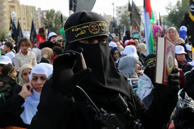 A female masked member of the Palestinian Al-Quds Brigades, the military wing of the Islamic Jihad group, holds a rifle, bullet and the Quran, Islam's holy book during a rally to commemorate the 29th anniversary of their group at the main square in Gaza City, Friday, Oct. 21, 2016. The Arabic on headband reads, \\\"No God but Allah and Muhammad is his messenger, Al-Quds Brigades \\\". (AP Photo/Adel Hana)
