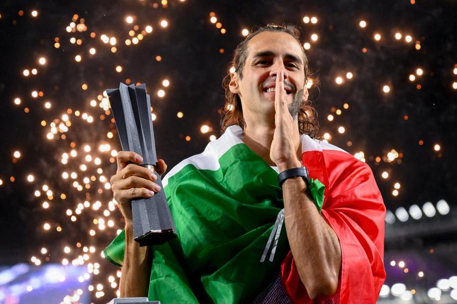 Gianmarco Tamberi, atleta italiano, salta in alto in un contesto di robot e tecnologia, con la sua famiglia e pubblico