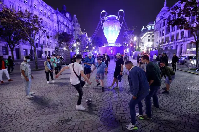 English Manchester City supporters and local people play with a football by a giant replica of the Champions League trophy in downtown Porto, Portugal, Friday, May 28, 2021. English clubs Manchester City and Chelsea will play the Champions League soccer final in Porto on Saturday. (AP Photo/Luis Vieira)