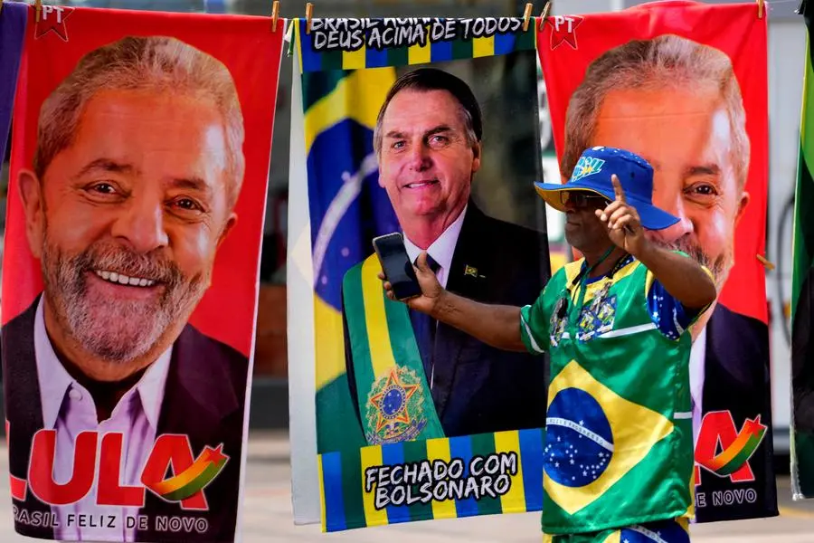 A demonstrator dressed in the colors of the Brazilian flag performs in front of a street vendor's towels for sale featuring Brazilian presidential candidates, current President Jair Bolsonaro, center, and former President Luiz Inacio Lula da Silva, in Brasilia, Brazil, Tuesday, Sept. 27, 2022. Nearly a dozen candidates are running in Brazilâ€™s presidential election but only two stand a chance of reaching a runoff: former President Luiz Inacio Lula da Silva and incumbent Jair Bolsonaro. (AP Photo/Eraldo Peres)