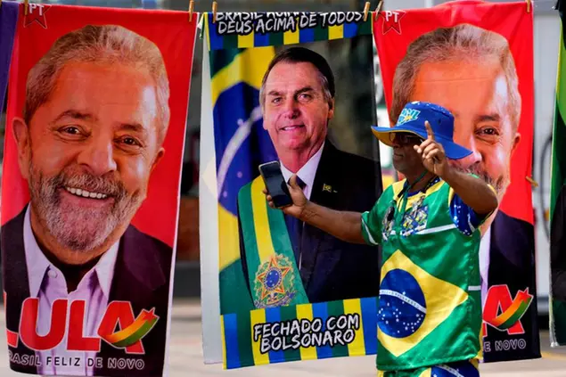 A demonstrator dressed in the colors of the Brazilian flag performs in front of a street vendor's towels for sale featuring Brazilian presidential candidates, current President Jair Bolsonaro, center, and former President Luiz Inacio Lula da Silva, in Brasilia, Brazil, Tuesday, Sept. 27, 2022. Nearly a dozen candidates are running in Brazilâ€™s presidential election but only two stand a chance of reaching a runoff: former President Luiz Inacio Lula da Silva and incumbent Jair Bolsonaro. (AP Photo/Eraldo Peres)