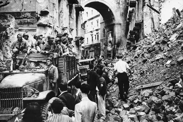 Advancing northward in their drive towards Rome, troop of the Allied fifth army are halted in a street in Naples on Dec. 9, 1943, while natives rush to clear away the debris to open a path wide enough to permit the passage of vehicles. (AP Photo)