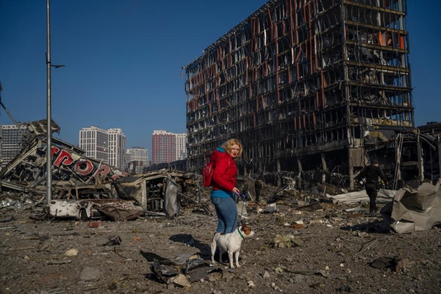 FILE - Irina Zubchenko walks with her dog Max amid the destruction caused after shelling of a shopping center, in Kyiv, Ukraine, Monday, March 21, 2022. The World Bank said Sunday, April 10, 2022 that Ukraine's economy will shrink by 45.1% this year because of Russia's invasion, which has shut down half of the country's businesses, choked off imports and exports and damaged a vast amount of critical infrastructure. (AP Photo/Rodrigo Abd, File)