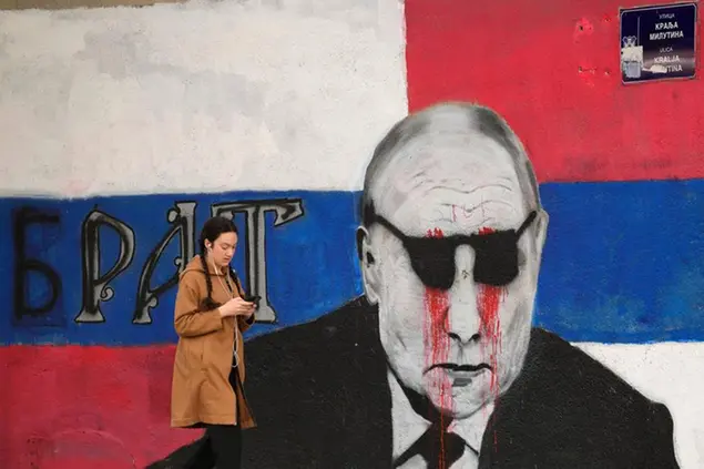 A woman passes by a mural depicting the Russian President Vladimir Putin that reads: ''Brother'' vandalized with paint, in Belgrade, Serbia, Saturday, May 7, 2022. Despite having to pay a big price Serbia for not introducing sanctions to Russia, Serbia will not do it , Serbian President Vucic said, but despite that the country will stay on its path toward the EU. (AP Photo/Darko Vojinovic)