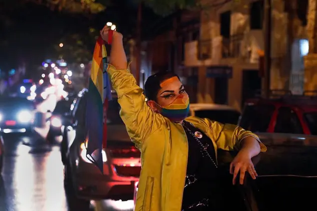 Wearing a mas to curb the spread of the new coronavirus, a trans person waves a flag from her car during a LGTBI Pride caravan in Asuncion, Paraguay, Wednesday, Sept. 30, 2020. LGTBI organizations celebrated their Pride day with a caravan of vehicles because of the ongoing COVID-19 pandemic. (AP Photo/Jorge Saenz)