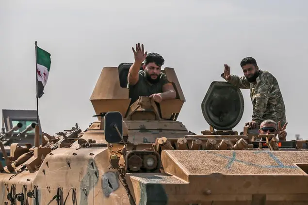 Due combattenti dell'opposizione siriana sostenuti dalla Turchia salutano mentre guidano per attraversare il confine con la Siria /Foto AP