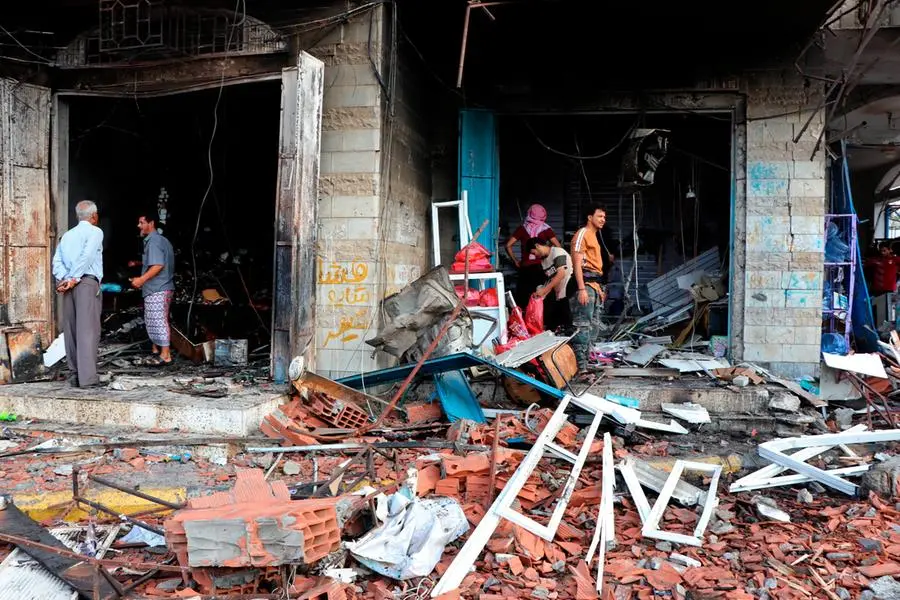 People stand amid debris at the site of a deadly car bomb attack close to a security checkpoint outside Aden’s international airport, in the neighborhood of Khormaksar, in the southern city of Aden, Yemen, Sunday, Oct. 31, 2021. Yemeni officials said at least eight people were killed by the car bomb that injured over 10 others. (AP Photo/Wael Qubady)
