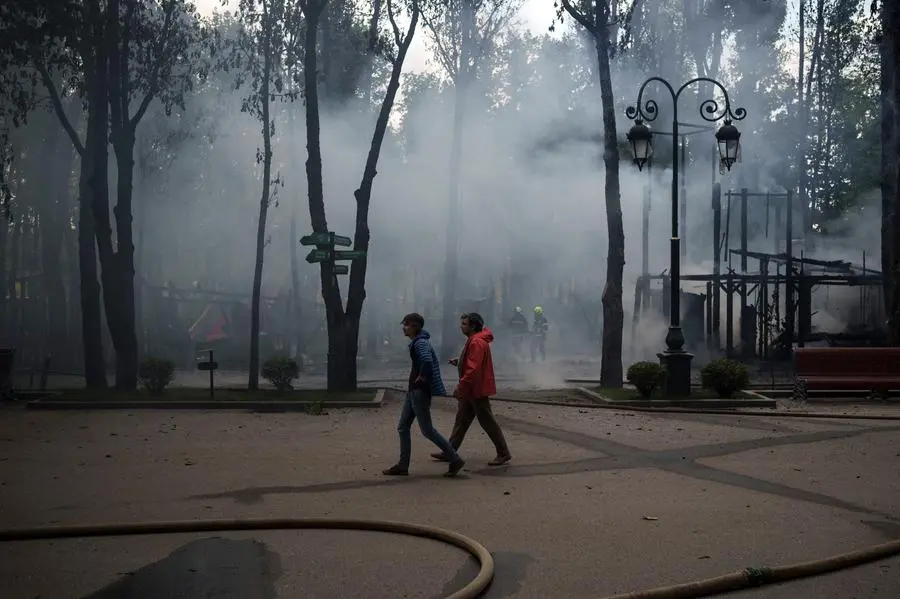 People walk at a local park as firefighters extinguish a fire following a Russian bombardment in Kharkiv, Ukraine, Tuesday, May 3, 2022. (AP Photo/Felipe Dana)