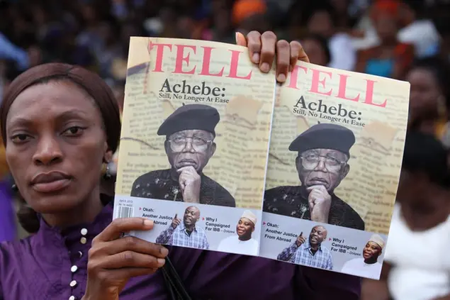 Una donna vende delle riviste con il ritratto dello scrittore Chinua Achebe, durante un evento in Nigeria, il 22 maggio 2013 (AP Photo/Sunday Alamba)