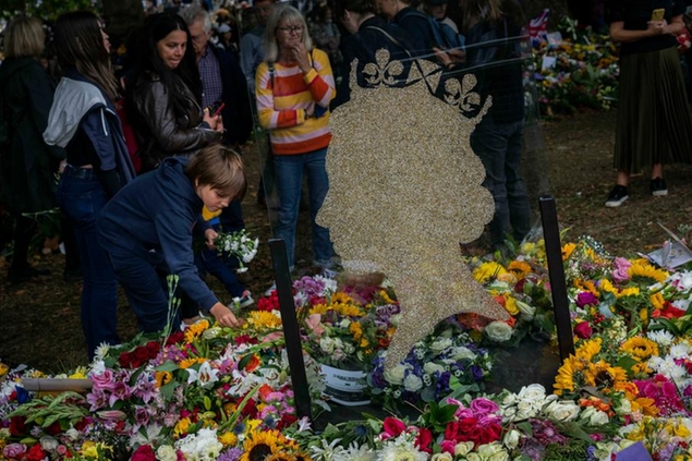 A child places flowers for Queen Elizabeth II at Green Park memorial next to Buckingham Palace in London, Thursday, Sept. 15, 2022. The Queen will lie in state in Westminster Hall for four full days before her funeral on Monday Sept. 19. (AP Photo/Bernat Armangue)