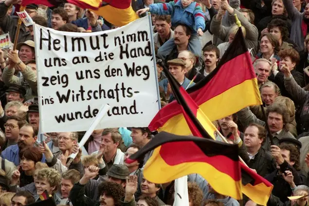 Supporters of the East German Alliance for Germany show a banner reading, \\\"Helmut, take our hand and show us the way to the wonderland of economy\\\", as Helmut Kohl, unseen, delivered a speech, during a rally on March 14, 1990, in Leipzig, Germany. Some 150,000 people took part in the event. (AP Photo/Heribert Proepper)
